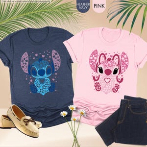 May include: Two t-shirts, one heather navy and one pink, featuring a decorative Stitch design. The navy shirt is paired with cream-colored loafers, while the pink shirt is next to a pair of dark blue jeans. The image also includes daisies.