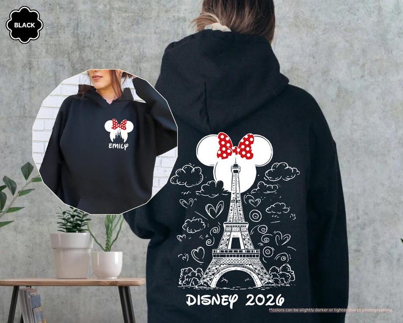May include: A black hooded sweatshirt featuring a white graphic on the back of the Eiffel Tower, clouds, hearts, and a Minnie Mouse ear silhouette with a red polka dot bow. The text reads DISNEY 2026. The front shows a small Minnie ear logo and EMILY.