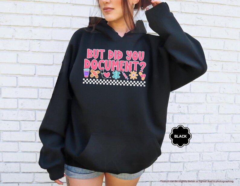 Puede incluir: Sudadera con capucha negra con el texto "BUT DID YOU DOCUMENT?" en rosa, rojo y azul. El dise&ntilde;o incluye iconos m&eacute;dicos y un borde a cuadros. Una etiqueta negra indica el color de la sudadera.