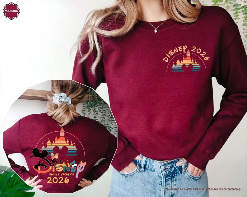 May include: Maroon sweatshirt with a Disney 2026 design. The design features a castle, Mickey and Minnie Mouse silhouettes, and the words "Disney Family Vacation 2026" in a colorful, arched layout. The sweatshirt has long sleeves.