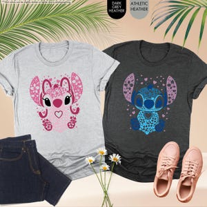 May include: Two t-shirts with a cartoon character design. One is light gray with a pink design, and the other is dark gray with a blue design. The designs feature a heart-shaped face and floral accents. A pair of blue jeans and pink sneakers are also visible.