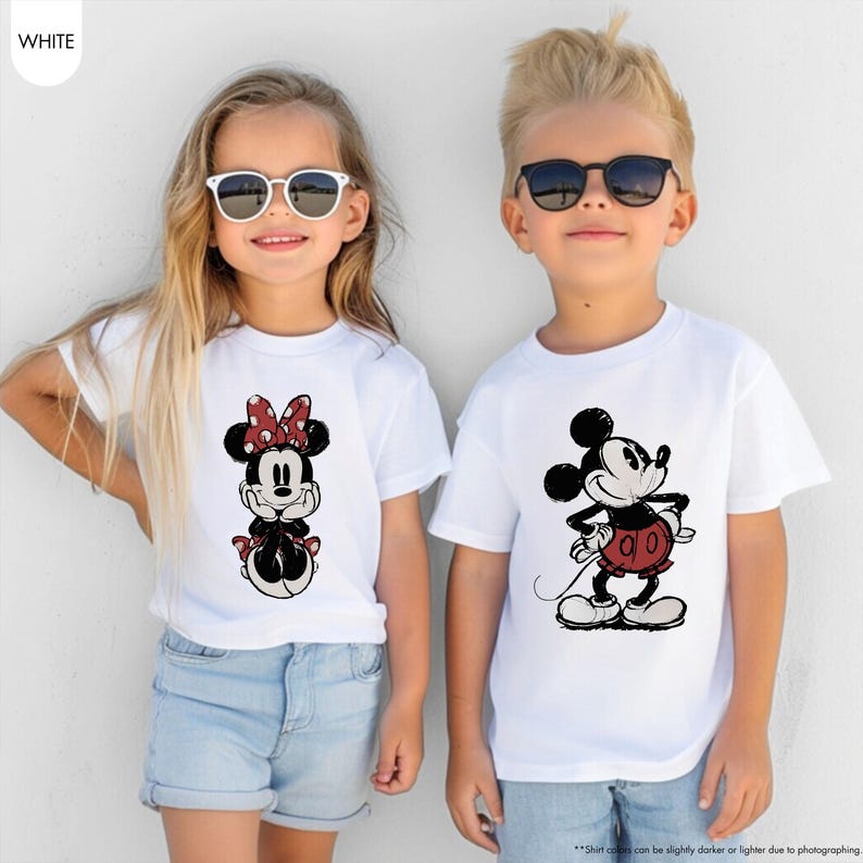 May include: Two children wearing white t-shirts with Disney character graphics. One shirt features Minnie Mouse with a red polka dot bow, and the other features Mickey Mouse in a red outfit. Both are wearing sunglasses.