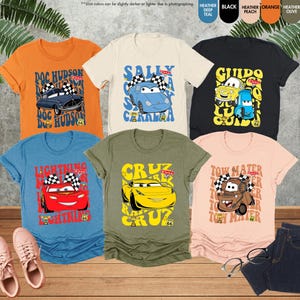 以下が含まれることがあります： 映画「カーズ」のキャラクターが描かれた、カラフルなTシャツのコレクション。オレンジ、青、黒、ピーチ、オリーブなど、さまざまな色があります。各シャツには、それぞれのキャラクターの名前と、チェッカーフラッグのデザインが表示されています。