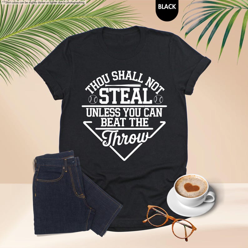 May include: Black t-shirt with the text "Thou Shall Not Steal Unless You Can Beat The Throw" in white. The shirt is paired with dark blue jeans, a cup of coffee with a heart design, and eyeglasses.