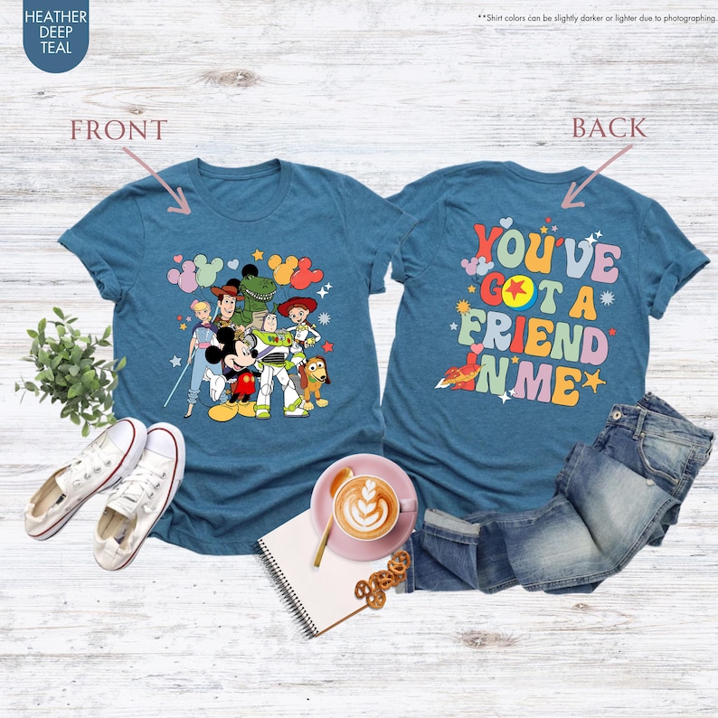 May include: Teal t-shirts with a cartoon graphic of Disney characters on the front and the phrase "YOU'VE GOT A FRIEND IN ME" on the back. The shirts are displayed with white sneakers and denim jeans.