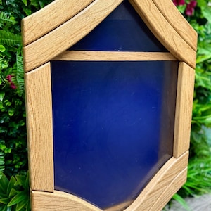 Può includere: Un espositore in legno con interno blu. La custodia ha un design a strati e angolato con finitura in legno naturale. L'espositore è ambientato su uno sfondo di fogliame verde.
