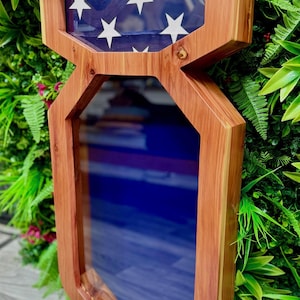May include: A wooden shadow box with a folded American flag in the top section and a blue background in the bottom section. The shadow box is made of cedar wood and has a rustic appearance.