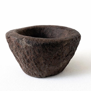 May include: A dark brown, hand-carved stone mortar with a rough, textured surface. The mortar has a wide, shallow bowl shape, perfect for grinding herbs and spices. The interior is a deep, dark brown.
