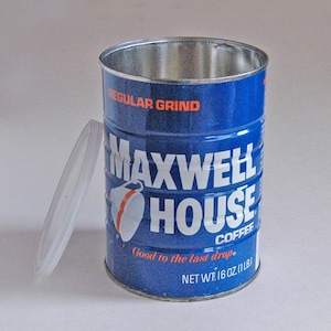 May include: A blue Maxwell House coffee can with the lid off, showing the interior. The can has the words "REGULAR GRIND" and "MAXWELL HOUSE COFFEE" printed on it. The can is labeled "NET WT. 16 OZ (1 LB)" and "Good to the last drop."
