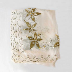 May include: A sheer off-white scarf featuring a scalloped edge with gold embroidery. The fabric is decorated with printed olive green leaf motifs and delicate gold sequin accents scattered throughout the floral-inspired pattern design.