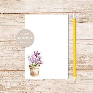 May include: A white notepad with a watercolor illustration of a potted purple crocus flower. The notepad is 4x6 inches and has 50 sheets.