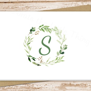May include: A white card with a green leafy wreath surrounding the letter "S" in the center.