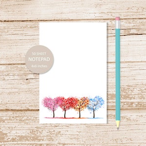 May include: A notepad with a watercolor illustration of four trees in different seasons. The trees are in a row and have heart-shaped leaves. The trees are pink, red, orange, and blue. The notepad is 4x6 inches and has 50 sheets.