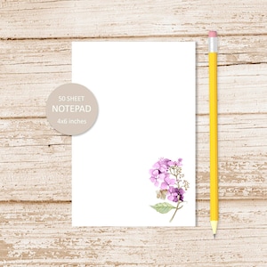 May include: A white notepad with a purple flower illustration and the text "50 SHEET NOTEPAD 4x6 inches".