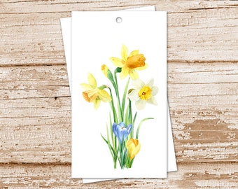 May include: Watercolor illustration of daffodils and other spring flowers on a white tag. The flowers are yellow, white, and blue with green stems and leaves. The tag has a hole at the top for hanging.