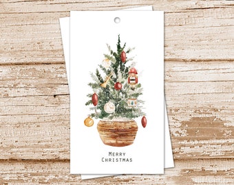 May include: Watercolor Christmas tree gift tags. The tags feature a decorated tree in a woven basket, adorned with ornaments and a nutcracker. The words "MERRY CHRISTMAS" are printed at the bottom. The tags are white with a hole at the top.