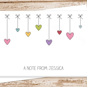 May include: A white card with a note that says "A note from Jessica". The card is decorated with a string of colorful hearts hanging from the top.