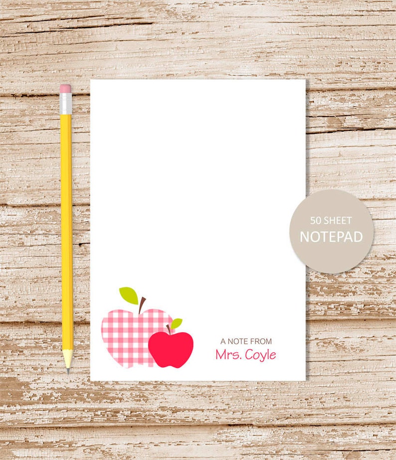 May include: A white notepad with a pink and white gingham apple and a red apple graphic. The notepad has the text "A note from Mrs. Coyle" and "50 sheet notepad".