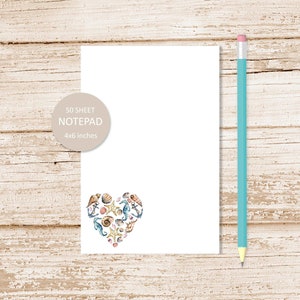 May include: A white notepad with a heart-shaped design made of seashells, starfish, and seahorses. The notepad is 4x6 inches and has 50 sheets.