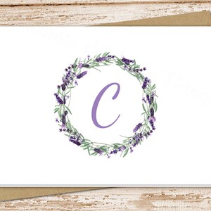 May include: A white card with a purple letter C in the center of a wreath of lavender flowers.