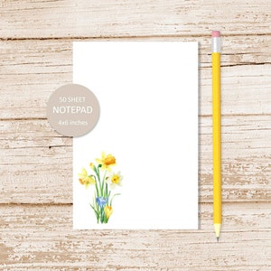 May include: A white notepad with a yellow pencil and a watercolor illustration of yellow daffodils and blue crocuses. The notepad is 4x6 inches and has 50 sheets.