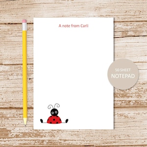 May include: A white notepad with a red ladybug illustration and the text "A note from Carli". The notepad is 50 sheets and has a beige label that says "50 SHEET NOTEPAD".