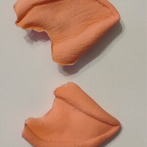 May include: Two peach-colored silicone ear molds, each with a small bite taken out of the top edge.