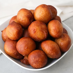 May include: A white bowl filled with a large amount of golden brown fried dough balls.