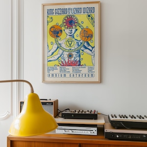 Op de afbeelding: Een ingelijste poster voor King Gizzard and the Lizard Wizard getiteld Omnium Gatherum. De gele print toont een centrale figuur met meerdere armen, een groot oog en dierenriemsymbolen. De tekst bevat songtitels en de naam van de band.