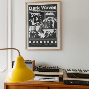 May include: A framed black and white poster titled "Dark Waves" with the subtitle "Post Punk Noise from the Underground." The poster is mounted on a white wall above a wooden cabinet. A yellow lamp and electronic music equipment are on the cabinet.