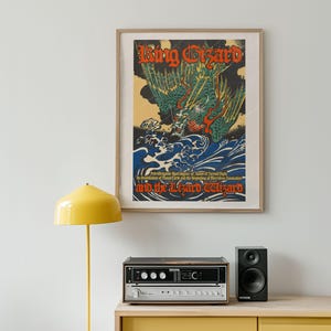 Op de afbeelding: Ingelijste poster met een vintage illustratie van een groene en rode draak, met de tekst "King Gizzard and the Lizard Wizard". Het kunstwerk toont blauwe golven en een gele achtergrond.