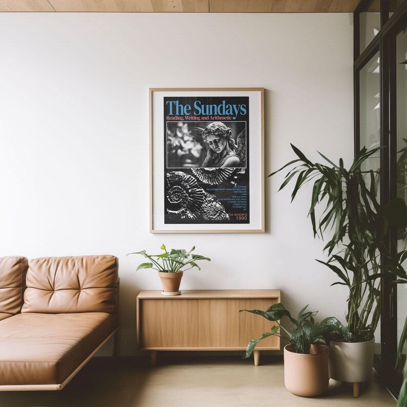 K&ouml;nnte beinhalten: Gerahmtes Poster mit dem Text "The Sundays" in Blau, mit einem Schwarz-Wei&szlig;-Bild einer Statue und Text. Das Poster befindet sich in einem hellen Holzrahmen und h&auml;ngt an einer wei&szlig;en Wand. Darunter befinden sich ein braunes Ledersofa und ein Holzschrank.