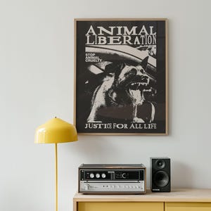 Può includere: Poster incorniciato con le parole "ANIMAL LIBERATION" e "JUSTICE FOR ALL LIFE". Il poster presenta un'immagine in bianco e nero di un cane. Una lampada gialla, uno stereo e un altoparlante sono su un mobile giallo.