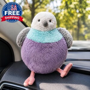 May include: A round plush bird toy featuring a white head, a teal chest, and a purple belly. The bird has dark gray wings, a small dark beak, and two light pink feet. The plush toy has a soft, fuzzy texture and a spherical body shape.