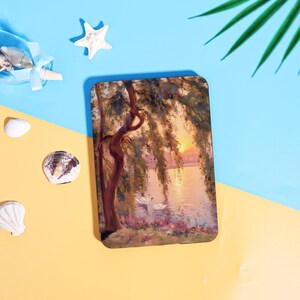 May include: A rectangular case featuring a serene landscape painting. The artwork depicts a sunset over a lake with two swans, a weeping willow tree, and colorful flowers. The case is surrounded by seashells and a starfish.