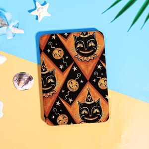 May include: A rectangular tablet case featuring a repeating pattern of black cats wearing party hats and smiling jack-o'-lanterns on an orange and black diamond background with small white stars scattered throughout the design.