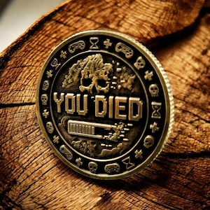 May include: A bronze-colored gaming coin with the words "YOU DIED" in pixelated font. The coin features a skull, a loading bar, and gaming-related symbols around the edge. The coin is set on a textured wooden surface.