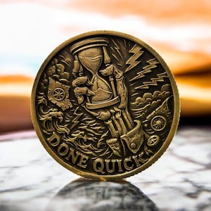 May include: Bronze coin with detailed relief work. The design includes an hourglass held by a skeletal hand, lightning, and the words "DONE QUICK". The coin has a vintage, antique appearance.