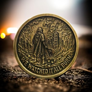 Puede incluir: Una moneda redonda de color bronce con un diseño en relieve detallado. La moneda presenta una figura encapuchada, un símbolo nuclear y un paisaje urbano en ruinas. El texto "WE WATCHED IT ALL BURN" está inscrito en el borde.