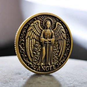 May include: A detailed, antique-style gold coin featuring an angel with outstretched wings, holding a sword. The word "ANGEL" is inscribed at the bottom. The coin has a detailed border with floral designs and a sunburst halo.