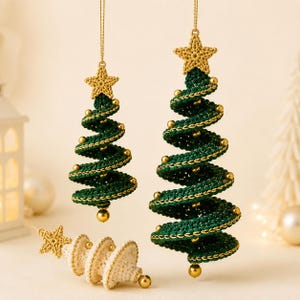 May include: Two hanging spiral Christmas tree ornaments in dark green crochet with gold metallic thread accents and gold beads, topped with a crocheted star. A third matching ornament in cream crochet lies horizontally below.