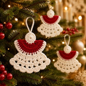 May include: Three handmade crochet angel ornaments featuring a cream-colored skirt and wings with a deep red bodice. Each ornament includes a small circular head and a matching cream-colored loop at the top for hanging on a tree branch.