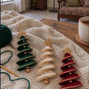 May include: Three spiral-shaped crochet Christmas tree ornaments in dark green, cream, and deep red. Each tree features a gold crocheted star at the top, small gold beads along the edges, and a gold jingle bell hanging from the bottom point.