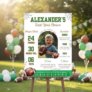 May include: A personalized sign for a first birthday, with the text "ALEXANDER'S First Year Down." The sign includes a photo of a child holding a football, along with stats: 24 pounds, 30 inches tall, and 6 teeth. The sign also lists favorite songs, food, toys, and things the child can do and loves.