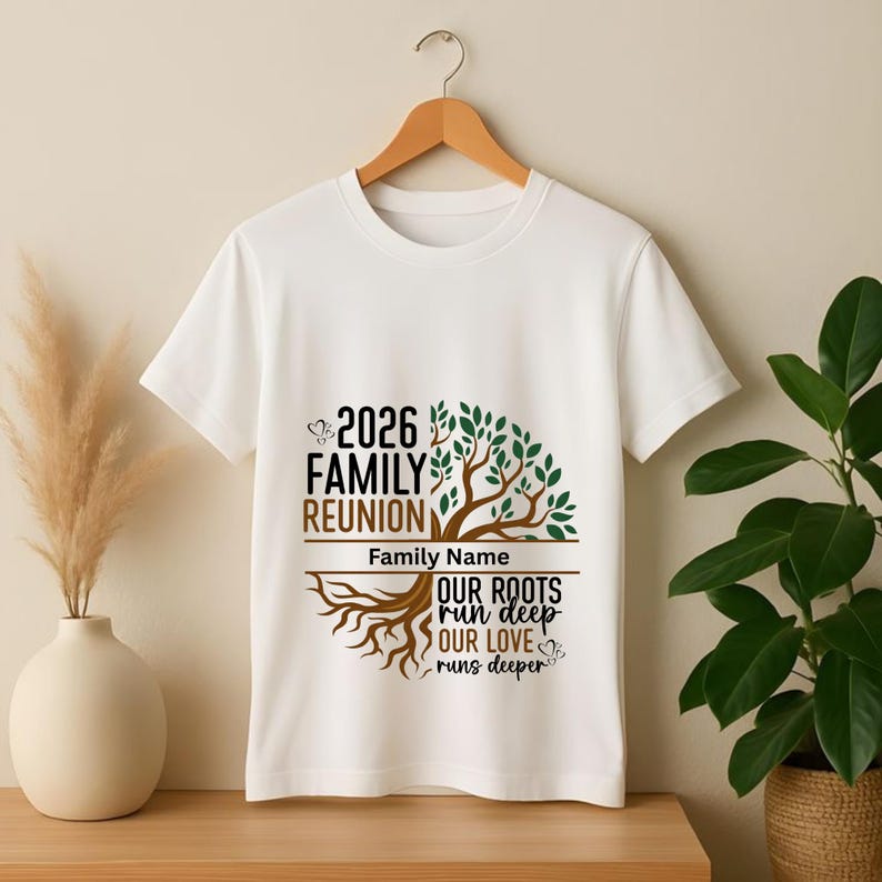 May include: White t-shirt with a family reunion design. The design includes the text "2026 Family Reunion", a tree graphic, and the phrase "Our Roots Run Deep, Our Love Runs Deeper". The shirt is hanging on a wooden hanger.