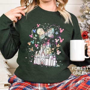 May include: Forest green sweatshirt featuring a colorful castle and mouse ears design. The graphic includes a bow and scattered colorful shapes. The text "FOREST GREEN" is at the bottom right.