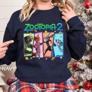 Peut inclure: Sweat-shirt bleu marine avec le texte "ZOOTOPIA 2" et un graphisme color&eacute; des personnages du film d'animation. Le graphisme comprend un paresseux, un renard, un lapin et un serpent. Le mot "NAVY" est imprim&eacute; en bas &agrave; gauche.