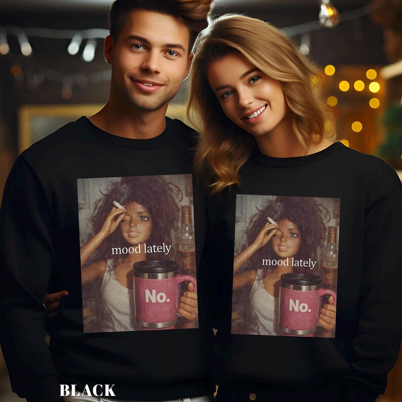 May include: A black crewneck sweatshirt featuring a graphic print of a doll with messy hair holding a cigarette and a pink travel mug with the text No. The print also includes the text mood lately in white lowercase letters centred above the mug.