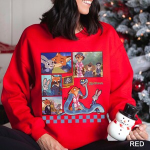 May include: A bright red long-sleeve sweatshirt featuring a graphic print of characters from the movie Zootopia. The design includes multiple panels showing scenes with Nick Wilde and Judy Hopps, along with a blue snake and the Zootopia logo.