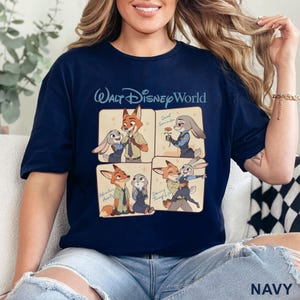 Puede incluir: Camiseta azul marino con un gr&aacute;fico de cuatro paneles de personajes de Zootopia. El panel superior tiene el texto "Walt Disney World" encima del gr&aacute;fico. El gr&aacute;fico muestra a Nick Wilde y Judy Hopps en varias poses. La palabra "NAVY" est&aacute; en la parte inferior derecha.